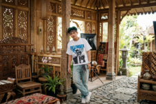 Young man in a white graphic T-shirt and bandana posing inside a carved wooden gazebo.