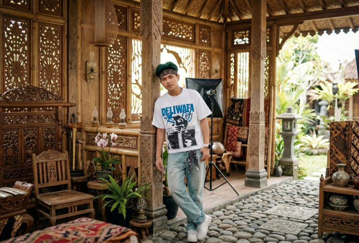 Young man in a white graphic T-shirt and bandana posing inside a carved wooden gazebo.