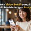 Wanita tersenyum di kafe memegang ponsel menampilkan logo Yandex; teks judul promosikan buka video diblokir dengan Proxy Yandex.
