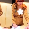 Two people in tan uniforms stand at a desk with papers; faces are censored and a white flower graphic covers a chest area on one person.