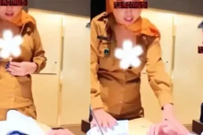 Two people in tan uniforms stand at a desk with papers; faces are censored and a white flower graphic covers a chest area on one person.