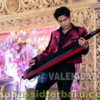 Male musician in a maroon jacket playing a red keytar on an ornate, flower-decorated stage backdrop.