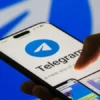 Hand holding a smartphone with the Telegram app open, showing the blue Telegram logo on screen.