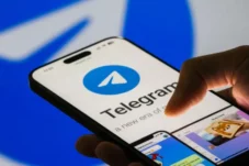 Hand holding a smartphone with the Telegram app open, showing the blue Telegram logo on screen.