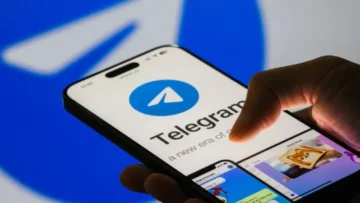 Hand holding a smartphone with the Telegram app open, showing the blue Telegram logo on screen.