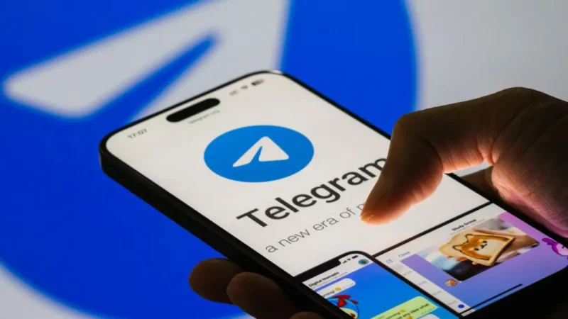 Hand holding a smartphone with the Telegram app open, showing the blue Telegram logo on screen.