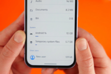 Smartphone screen showing storage settings: Android 16 uses 10 GB, Temporary system files 5.7 GB, New user 139 kB, with an orange background behind the device.
